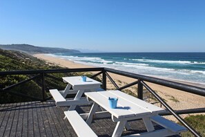 A wooden deck with picnic tables and benches overlooking a beach with waves. - The Dunes Resort 80 (Keurboomstrand)