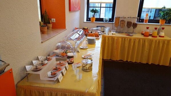 A buffet setup with various food items and condiments, including a clear glass jar of Nutella, a fruit bowl, and a spread of cheeses. - Hotel Trutzpfaff (Speyer)