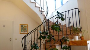 Una escalera con barandilla de hierro forjado, plantas en macetas y un cuadro en la pared.