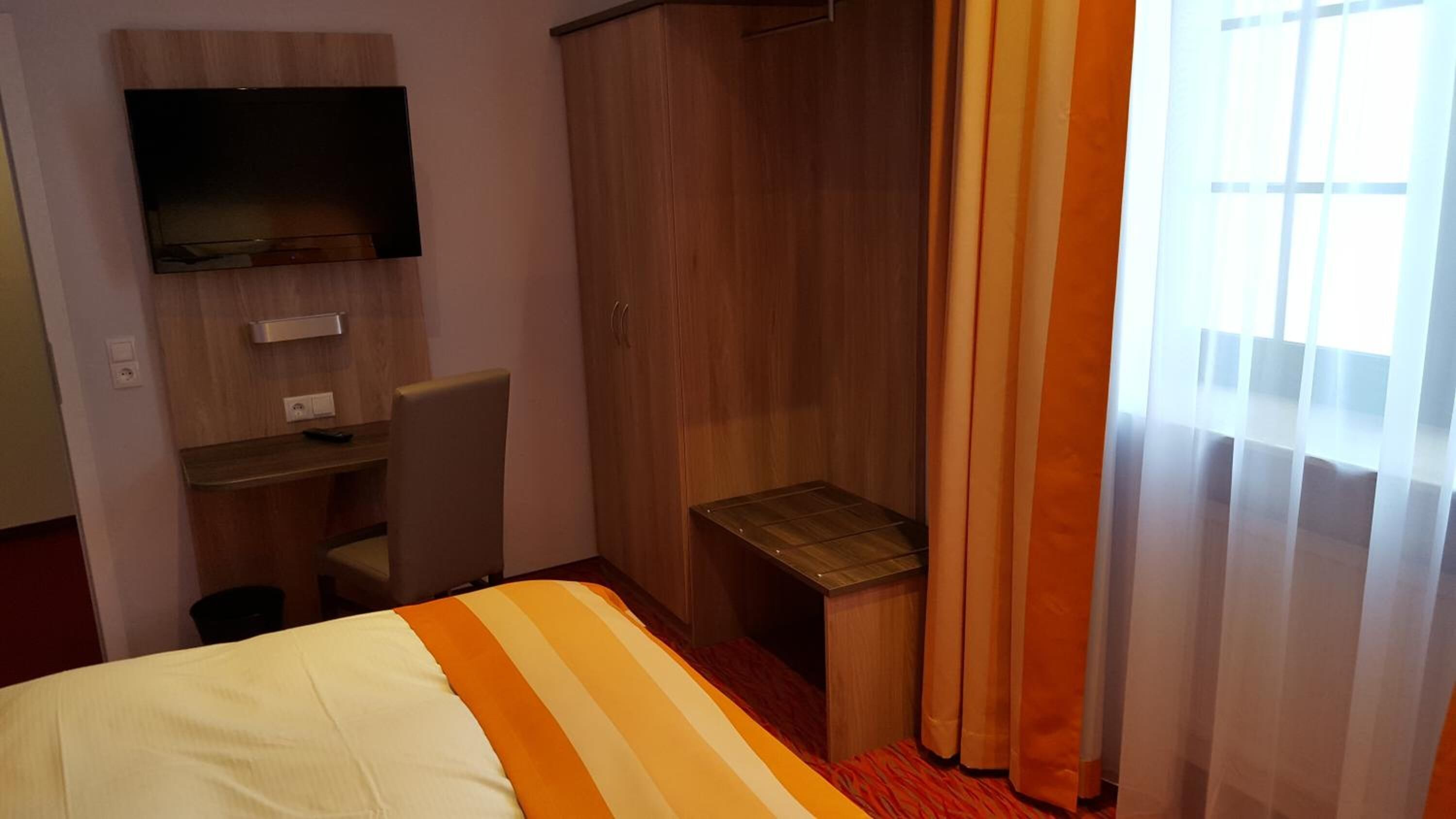 Ein Hotelzimmer mit Bett, Schreibtisch, Stuhl, Fernseher und einem fensterbepflanzten Fenster.