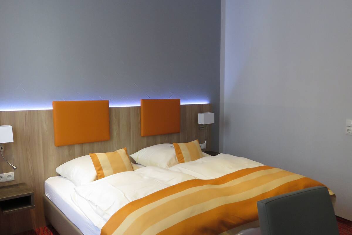 A hotel room with a bed, bedside tables, a desk, and a chair.