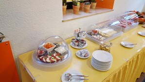Una mesa de buffet con diversos alimentos, incluyendo una campana de vidrio con tomates y mozzarella en rodajas, una bandeja de quesos variados y un recipiente con bombones dorados.