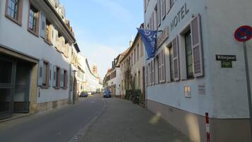 Una calle estrecha con un hotel llamado "Hotel Webergasse" a la derecha. Hay coches estacionados en la calle y una bandera azul es visible.