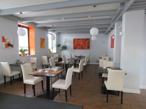 A spacious dining area with multiple tables and chairs, large windows, and hanging pendant lights. - Hotel Trutzpfaff (Speyer)