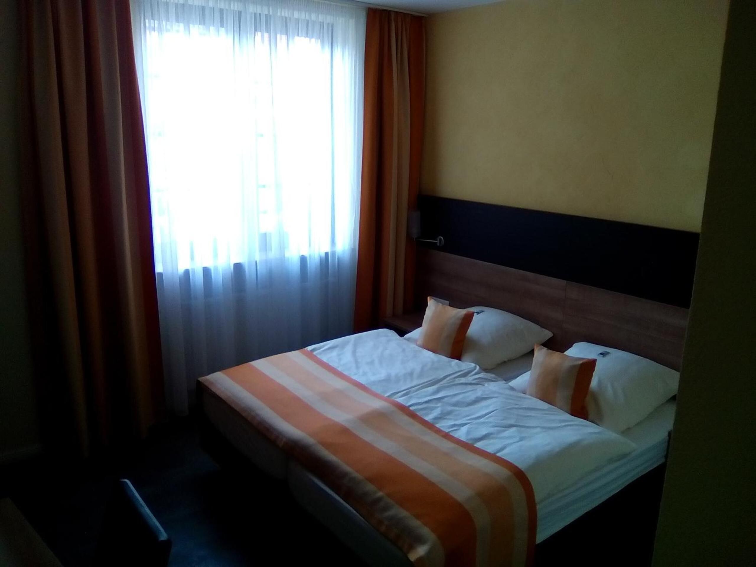 A hotel room with a bed, curtains, and a window.