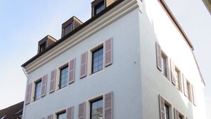 Un edificio de hotel con numerosas ventanas y contraventanas, un letrero que indica que es un hotel, y una bandera.