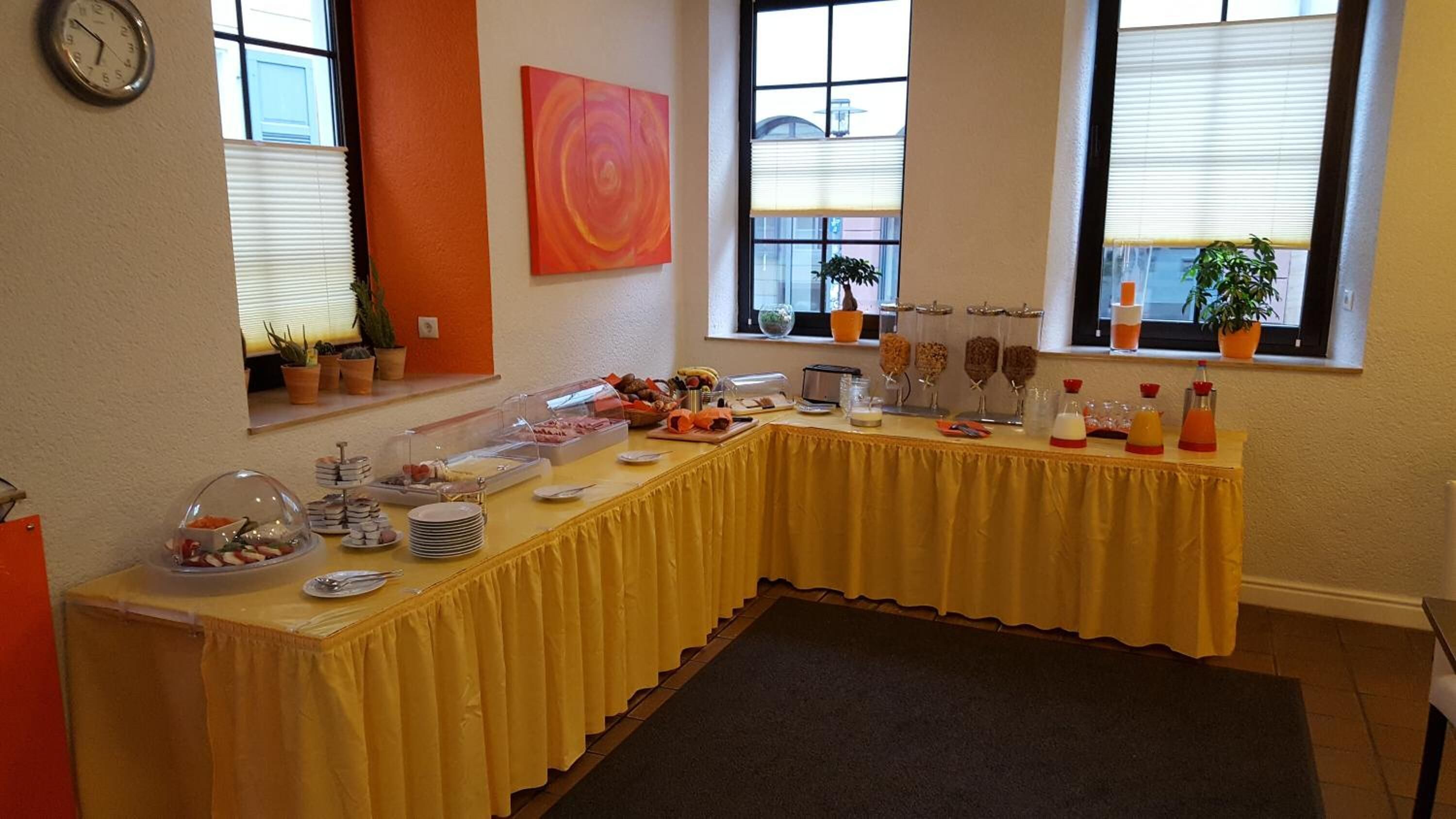 Een buffetopstelling met diverse gerechten en toevoegingen, een klok aan de muur en potplanten bij de ramen.