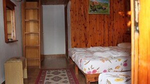 Une chambre avec une armoire en bois, un lit avec une literie à motifs floraux et un petit tabouret.