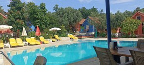 Una piscina con sillas de descanso amarillas y sombrillas, rodeada de edificios coloridos y árboles.