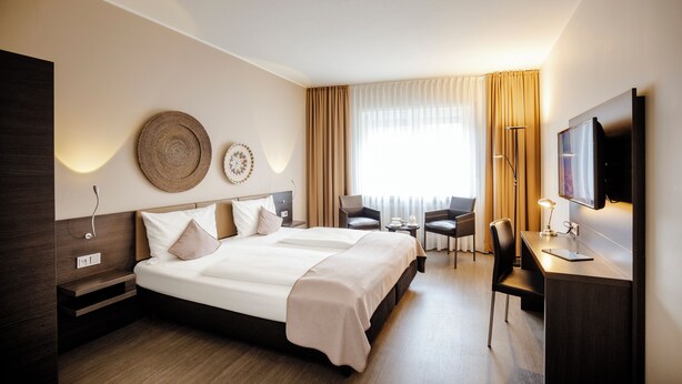 A modern hotel room with a large bed, a desk, a chair, and a TV.