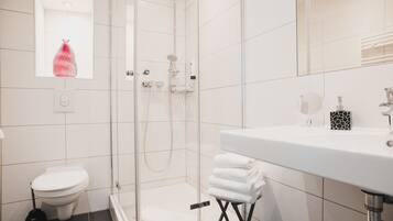 Un baño moderno con ducha de vidrio, inodoro blanco y lavamanos con espejo.
