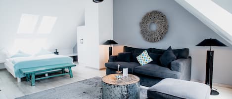 Un dormitorio moderno con cama, un sofá gris, una mesa redonda y un ventanal grande.