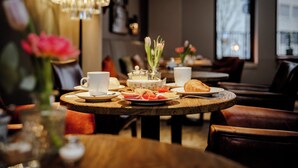 A dining table with plates of food, a teapot, and cups, set in a room with a chandelier and a window.