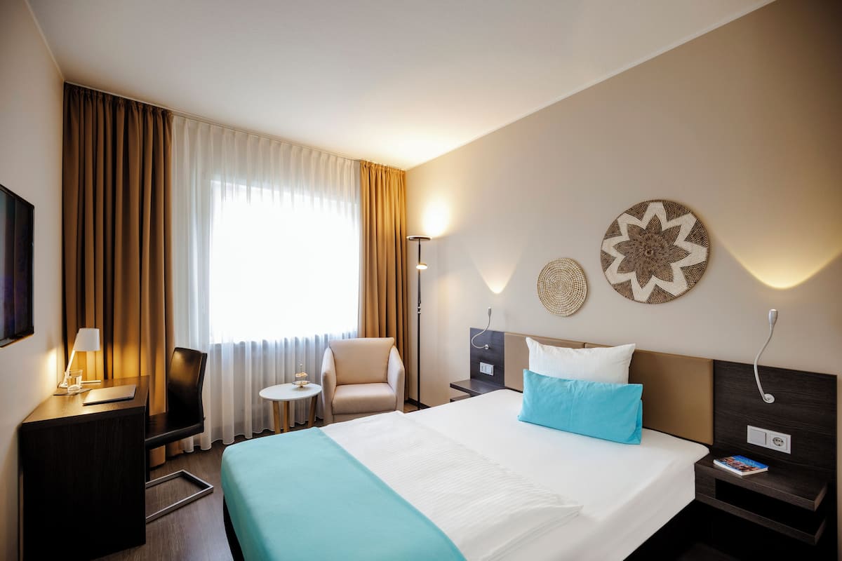 Ein Hotelzimmer mit Bett, Schreibtisch, Stuhl, Nachttisch und Lampe.