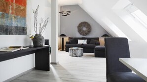 A modern loft apartment with a sloped ceiling, a black sofa, a round coffee table, and a large window.