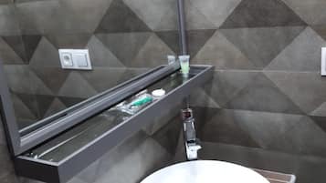 A bathroom with a modern design, featuring a round sink, a mirror, and a shelf with toiletries.