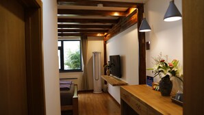 A hallway with wooden flooring, a sofa, a television, a vase with flowers, and pendant lights. - Beijing Downtown Travelotel (Beijing)