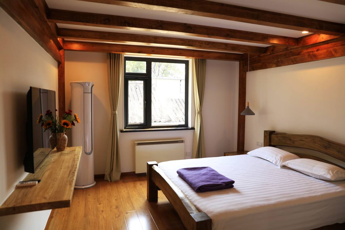 A bedroom with a wooden bed, a bedside table with a vase of flowers, a radiator, and a window with curtains.
