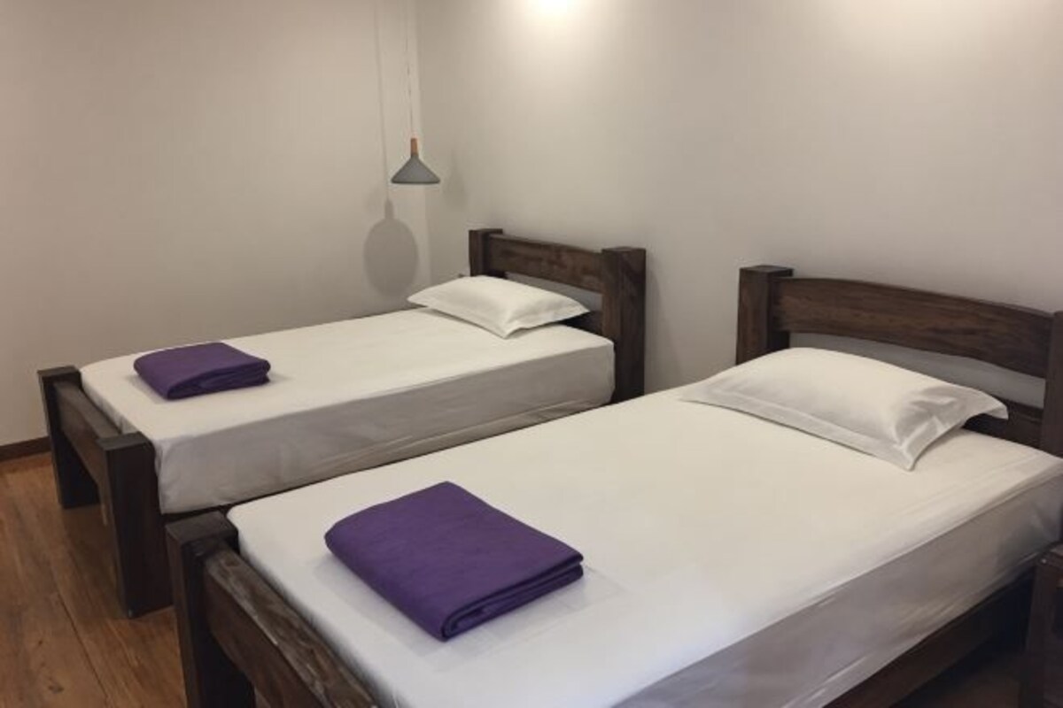 Two single beds with wooden frames, white bedding, and purple towels.