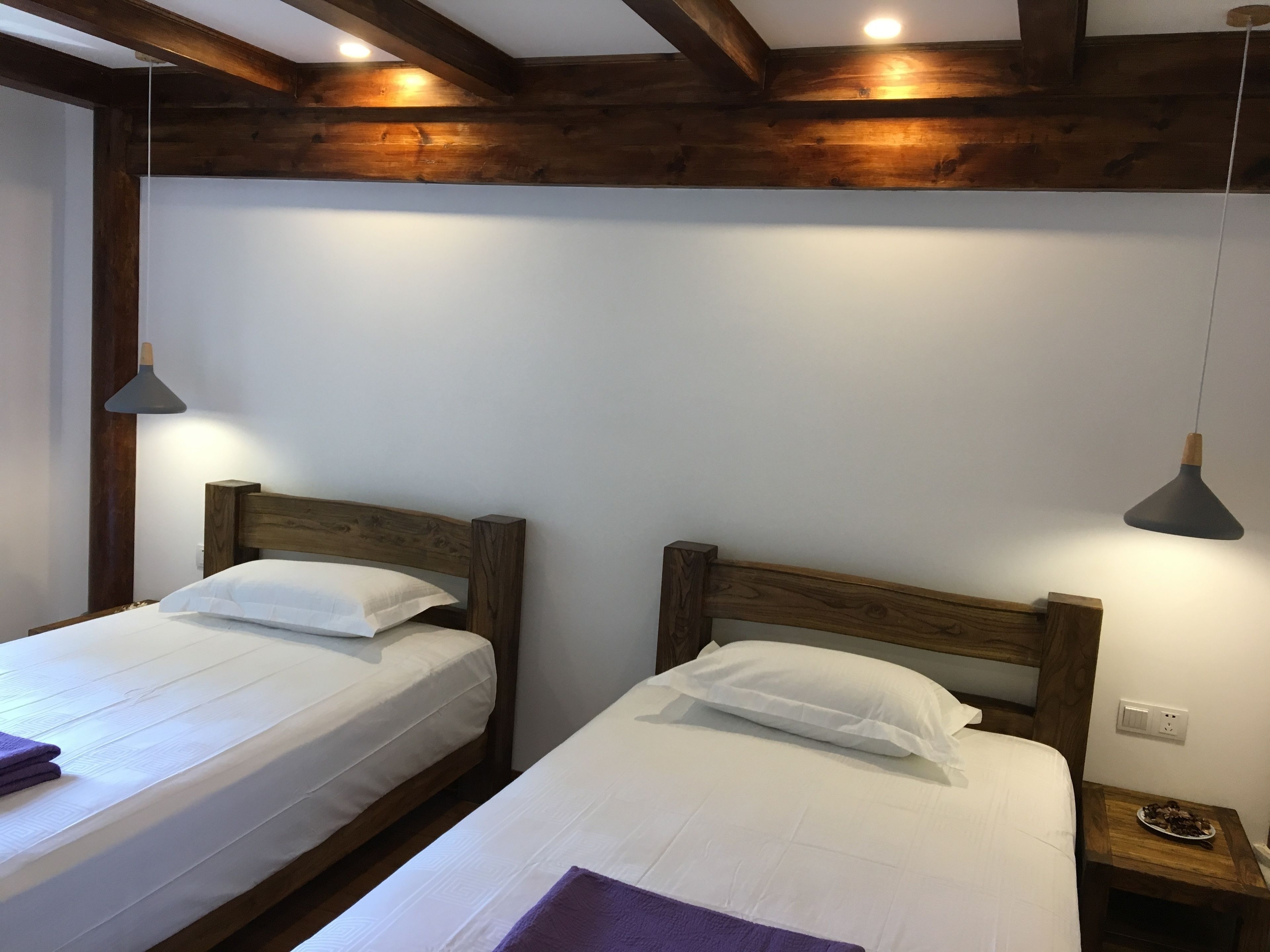 Due letti singoli con testiere in legno e biancheria bianca, un comodino in legno con un piatto di cioccolatini e un lampadario a sospensione.