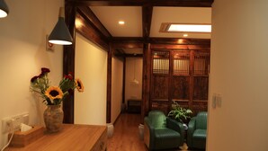 A room with a wooden floor, a wooden desk with a vase of flowers, two green chairs, and a traditional wooden screen. - Beijing Downtown Travelotel (Beijing)