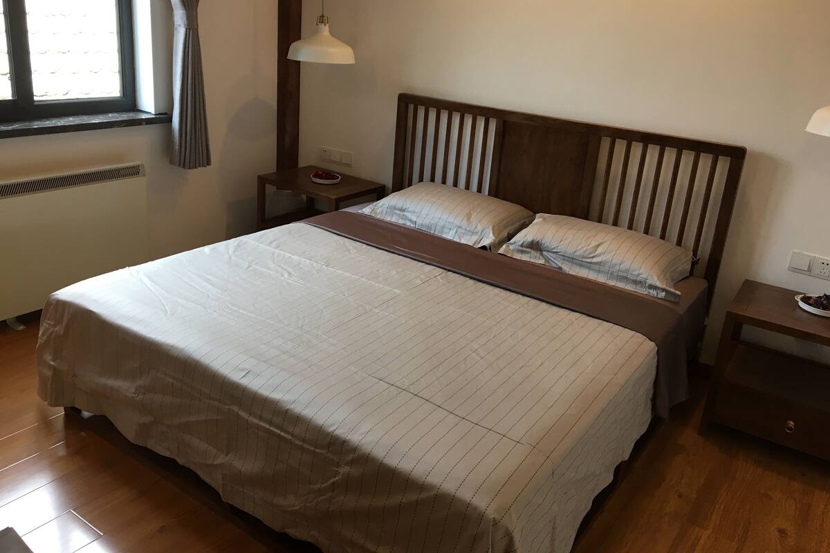 A neatly made bed with a striped bedspread, a wooden headboard, and two bedside tables with lamps.