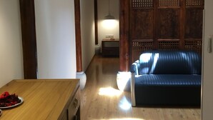 A room with a wooden floor, a blue sofa, a wooden table with a lamp, and a wall with a decorative panel. - Beijing Downtown Travelotel (Beijing)