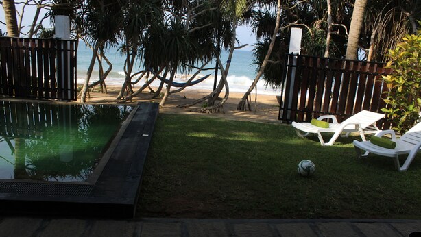 A pool area with a view of the beach, a hammock, and two lounge chairs. - Villa 948 Beach Front with Pool (Hikkaduwa)
