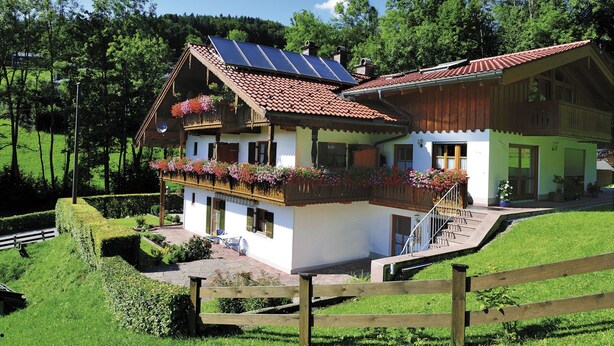 A traditional chalet with a sloped roof, solar panels, and a balcony with flower boxes. - Gaestehaus Vogl (Berchtesgaden)