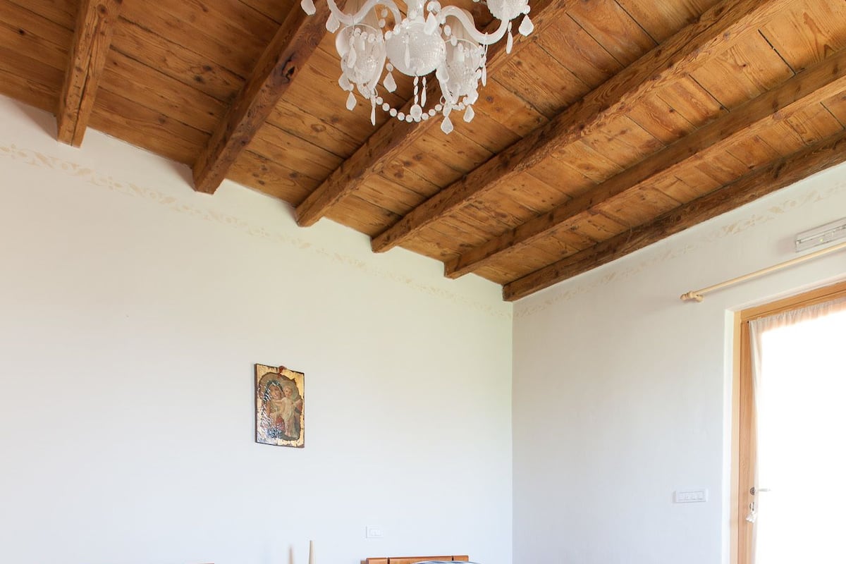 A room with two wooden beds, a colorful striped rug, and a wooden ceiling with exposed beams.