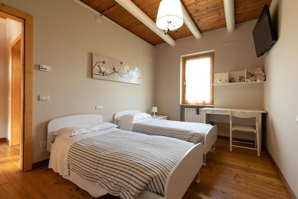 A bedroom with two beds, a desk, a TV, and a window.