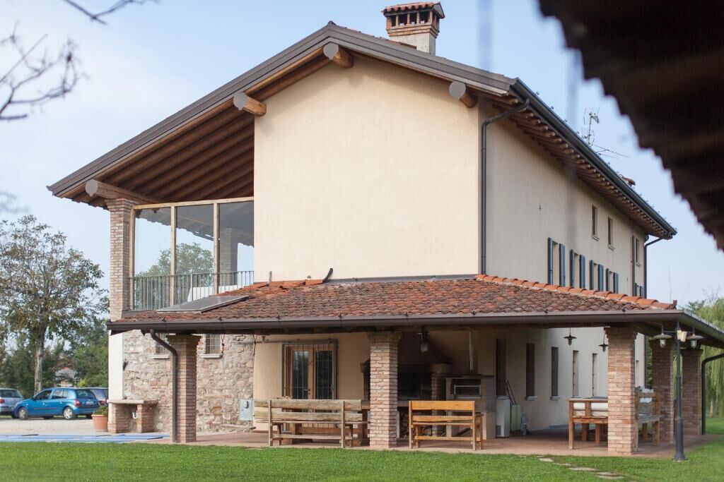 A two-story house with a covered patio area, stone pillars, and a tiled roof.
