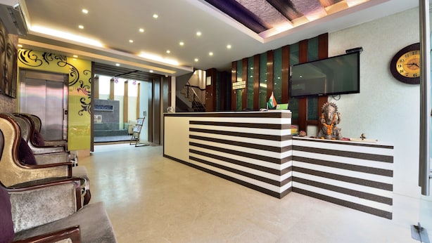 A hotel reception area with a modern design, including a reception desk, seating area, and a large flat-screen TV. - Hotel Taksh Inn (New Delhi)