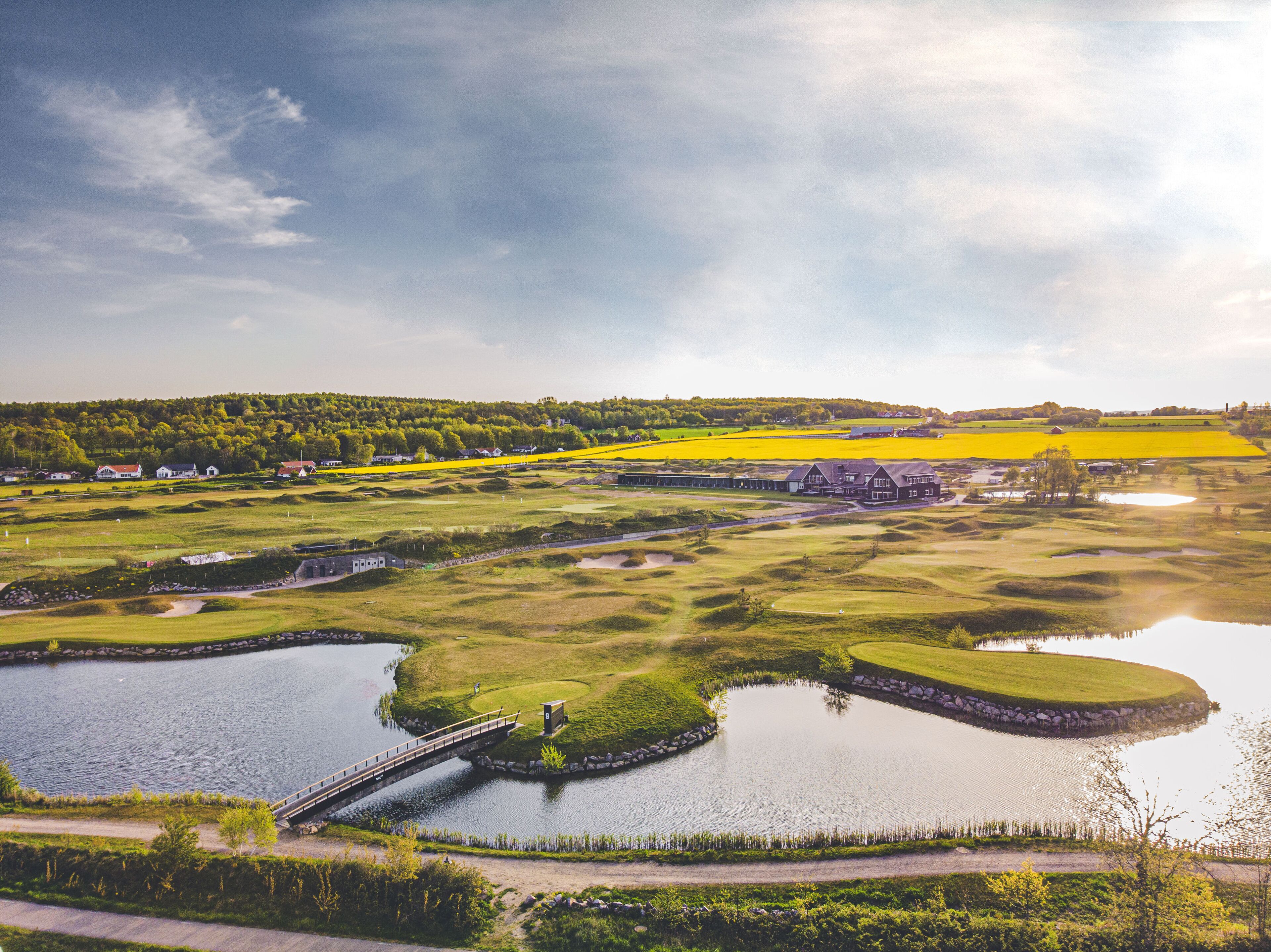 Un campo de golf con un puente, cuerpos de agua y vegetación circundante.