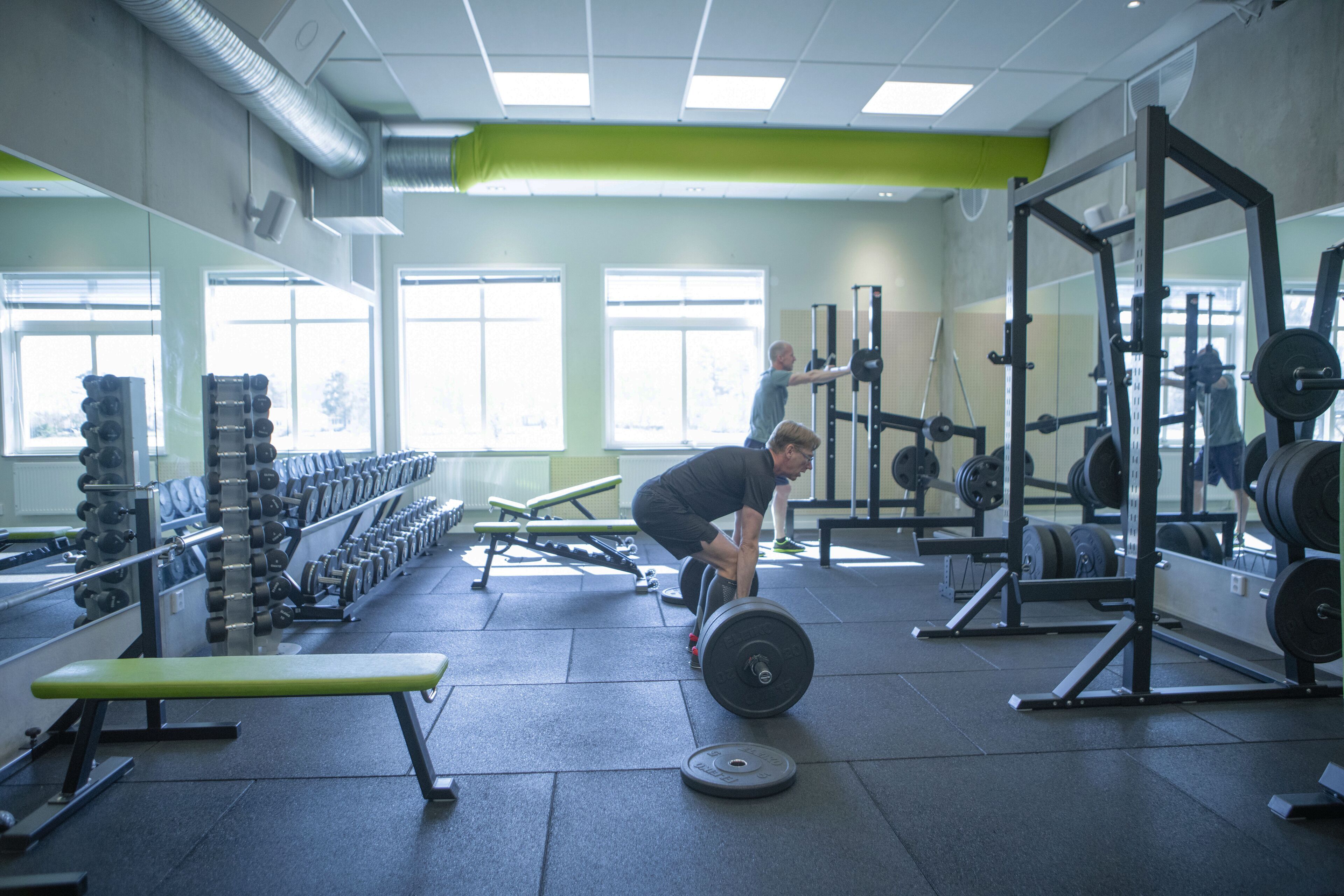 Une salle de sport équipée de matériel de musculation, de bancs et dotée d’un mur recouvert de miroirs.