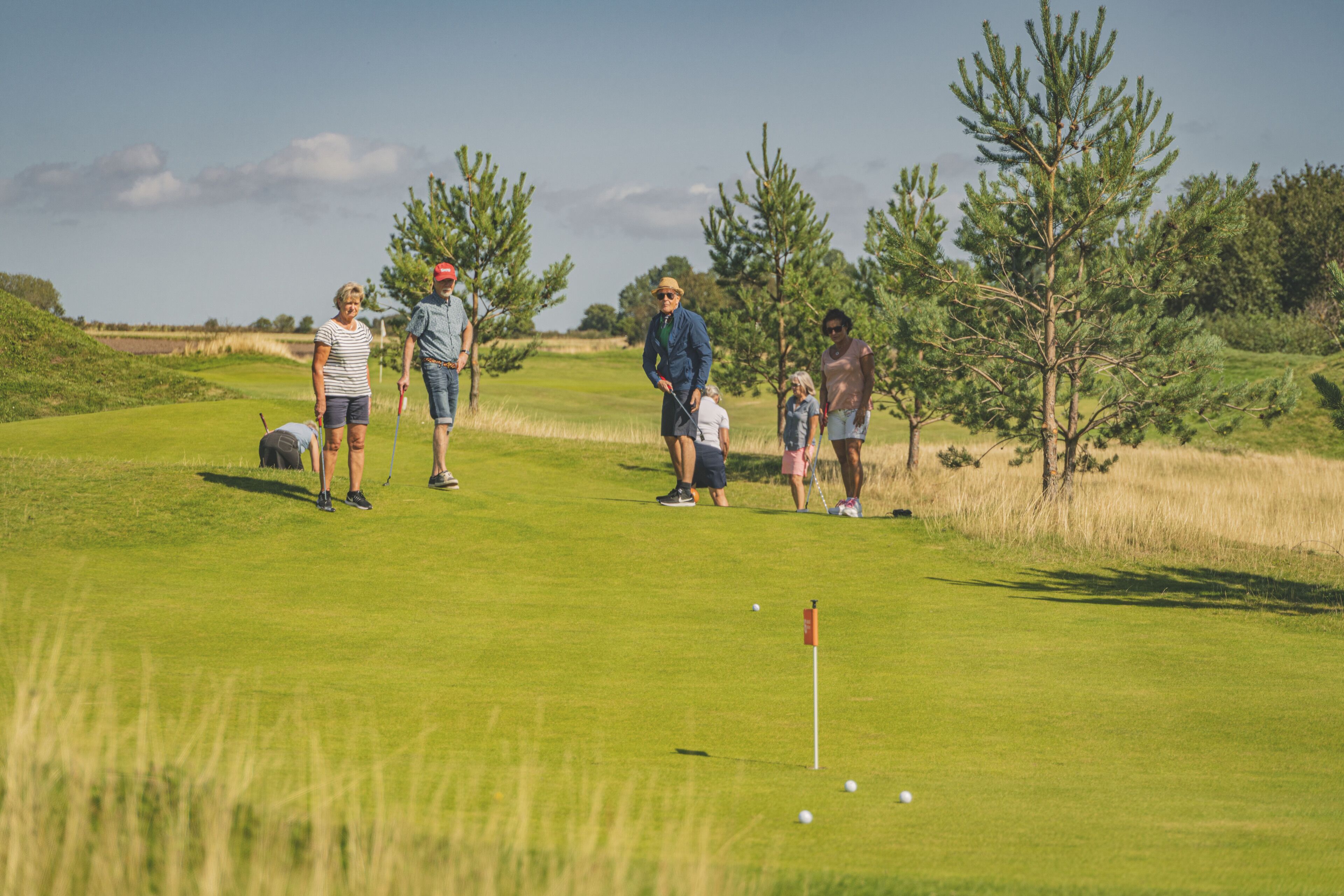 A golf course with a putting green, trees, and a clear sky.