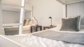 Een moderne hotelkamer met een stapelbed, een nachtkastje met een lamp, een klein nachtkastje, en een groot bed met een grijze plaid.