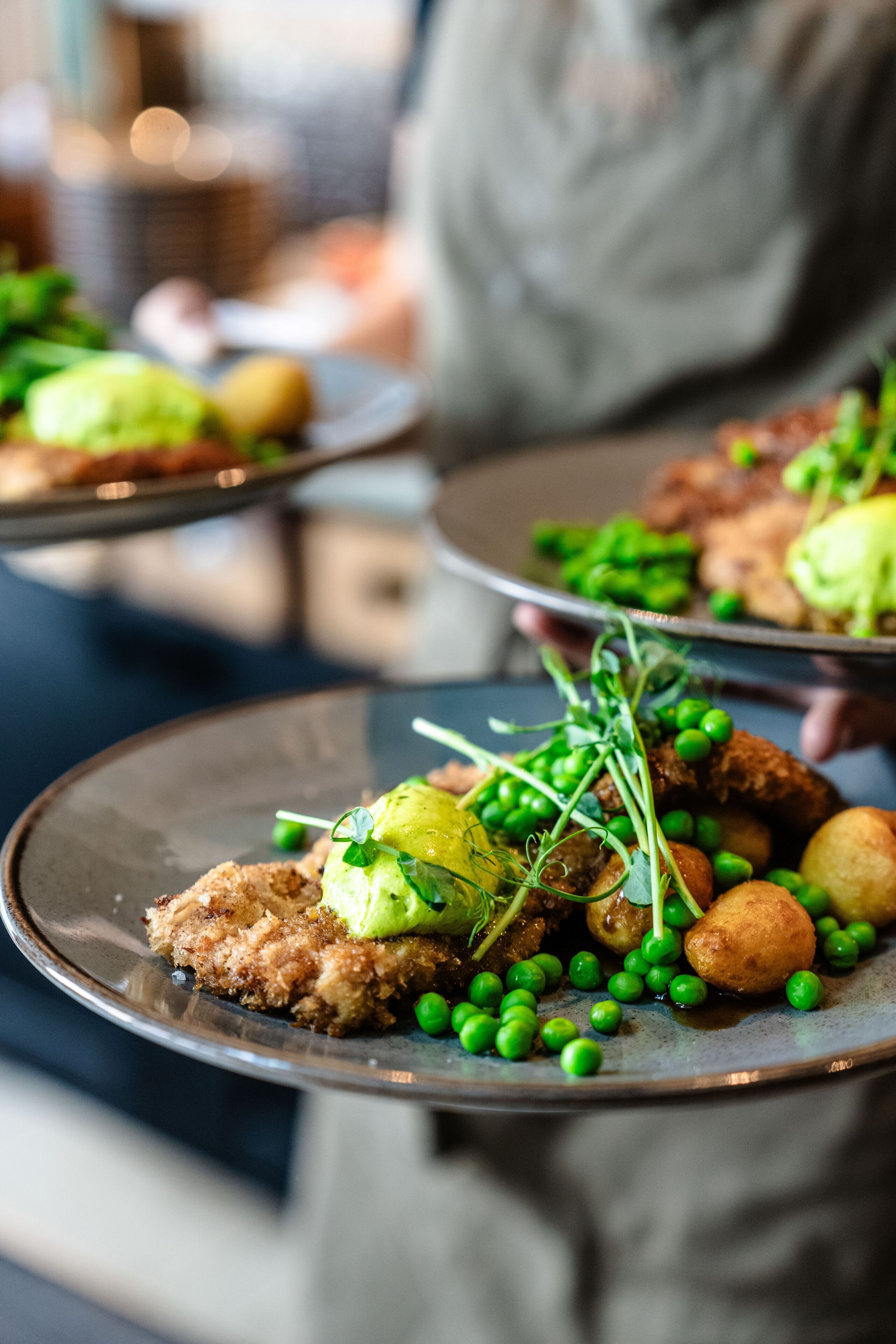A plate of food with peas, potatoes, and a piece of meat, served on a ceramic plate.