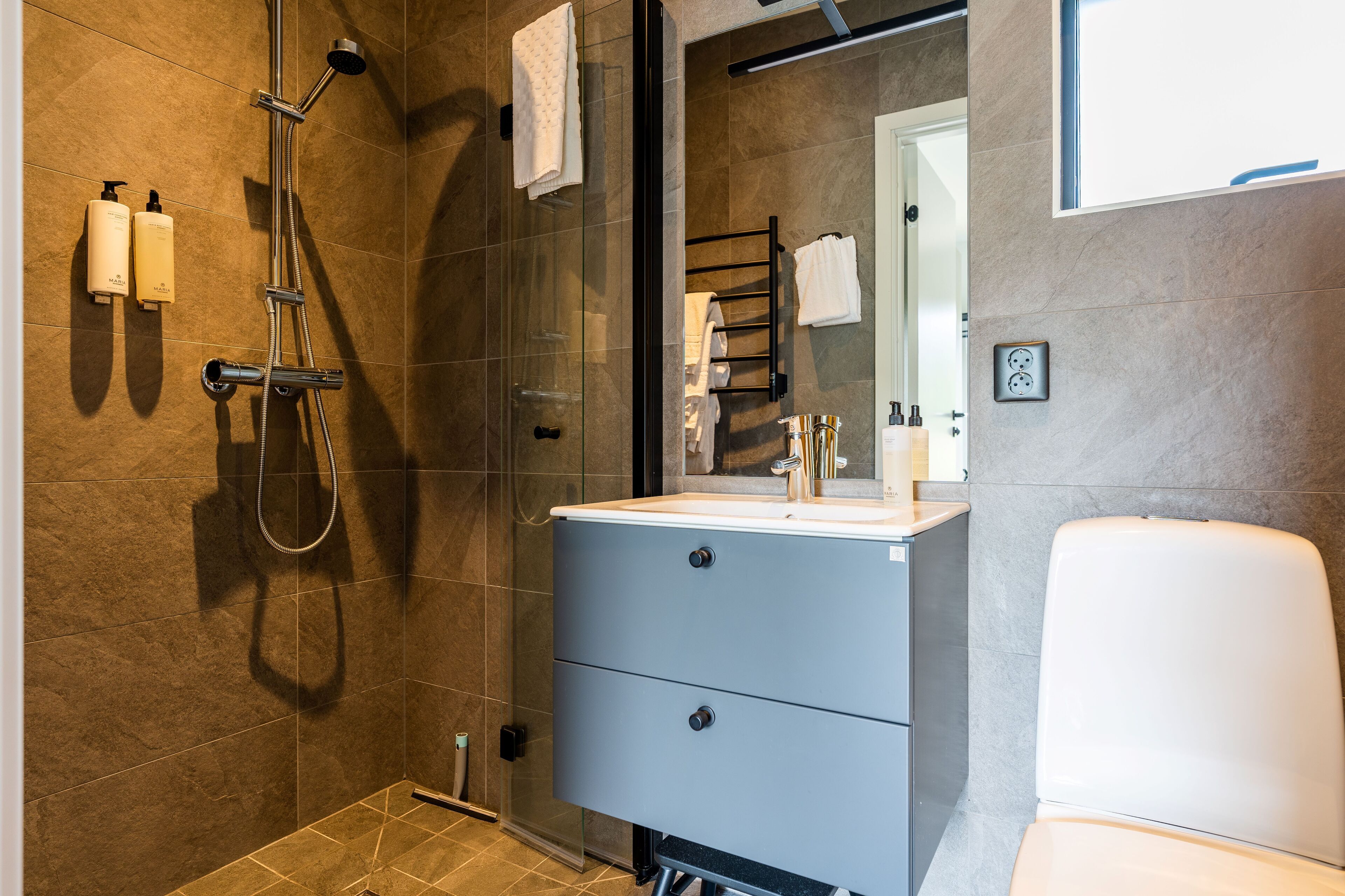 Un baño moderno con ducha de vidrio, un lavabo blanco y un inodoro.