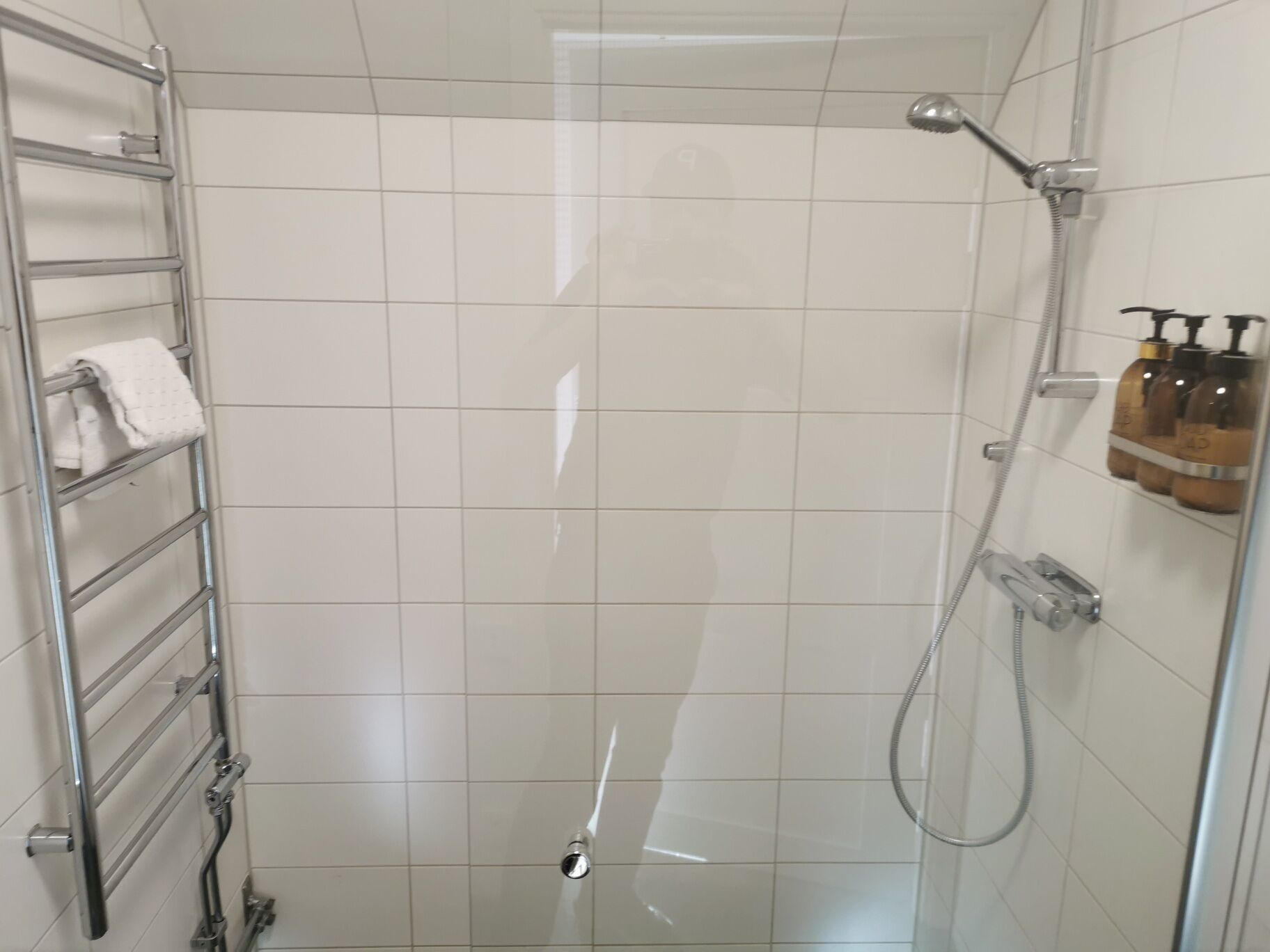 Ducha con puerta de vidrio, toallero con una toalla doblada y dispensador de jabón en la pared.