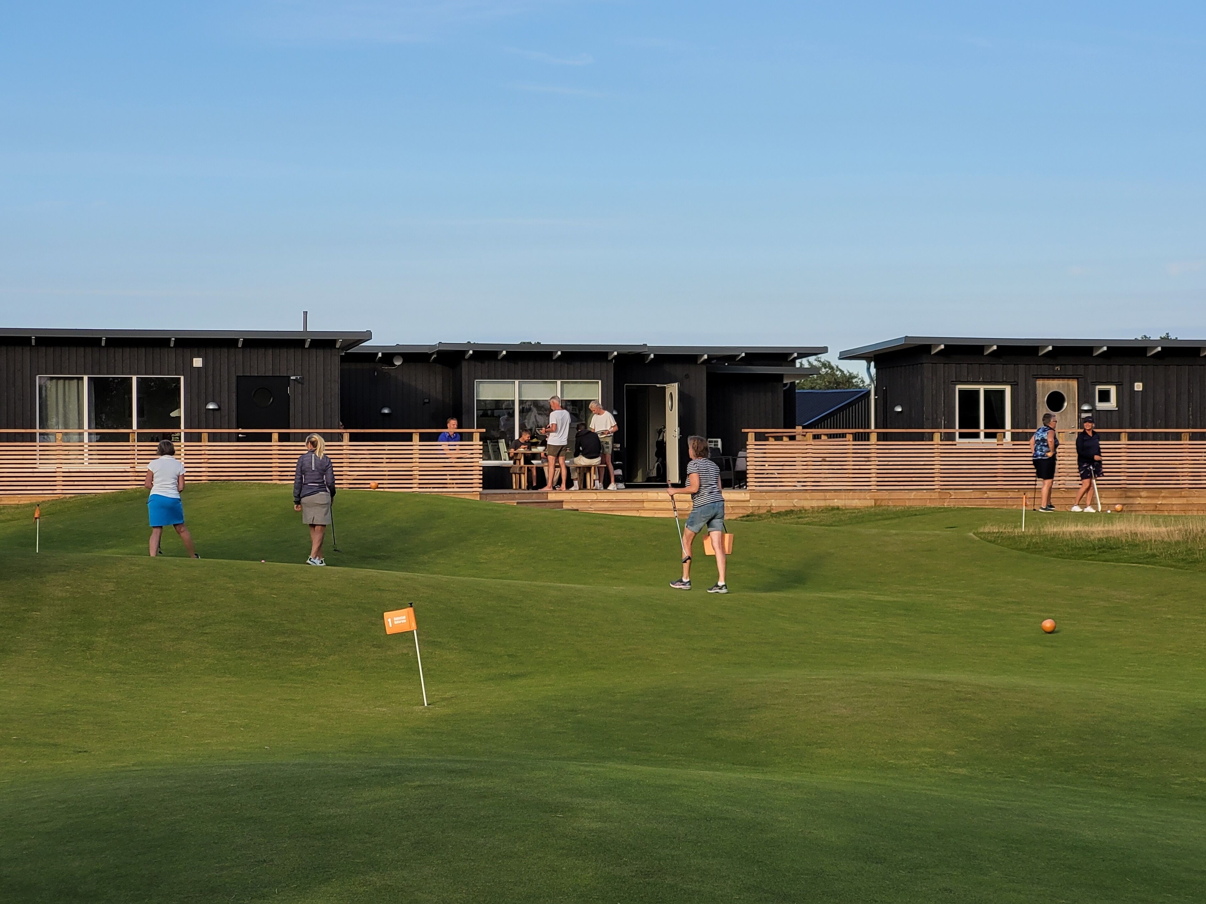 A golf course with a modern clubhouse, a putting green, and a flag marking the hole.