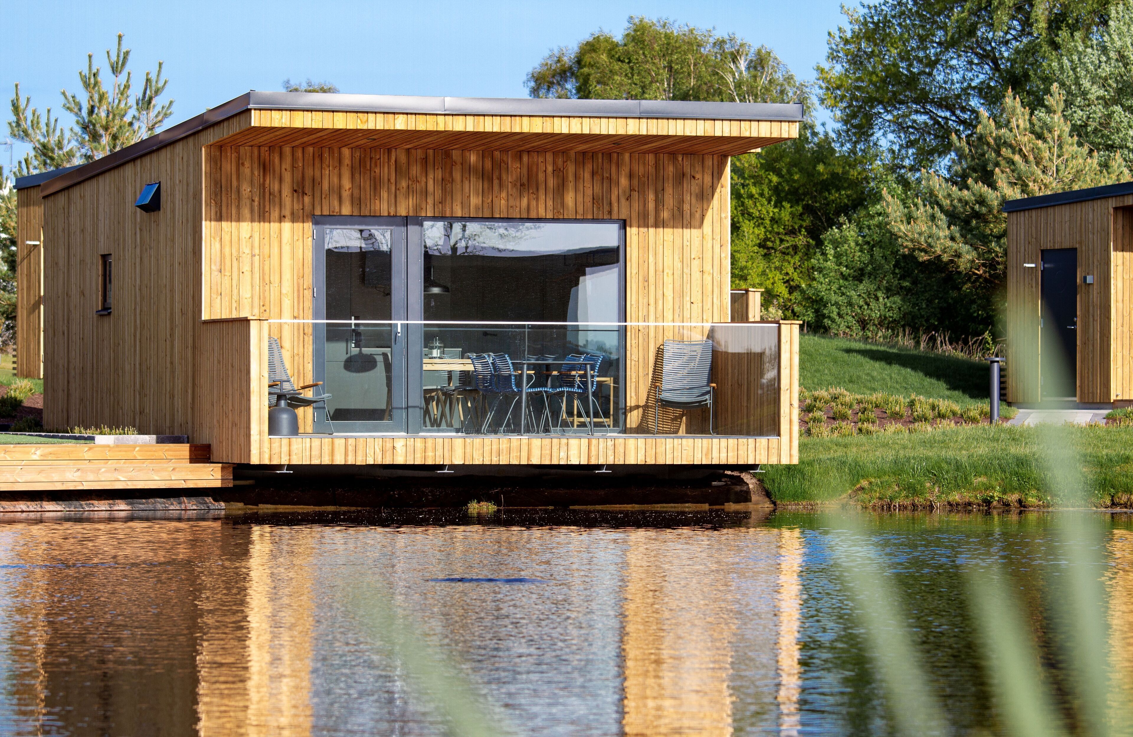 Una estructura flotante de madera con balcón de cristal, una mesa y sillas.