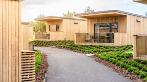 Ein modernes Holzgebäude mit gepflastertem Weg und kleinen, grünen Sträuchern.