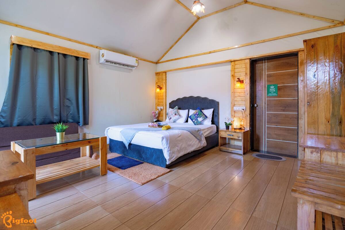 A wooden-floored bedroom with a bed, a nightstand, a glass coffee table, and a sofa.