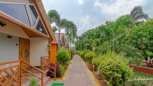 A pathway leading to a building with a wooden staircase and railing, surrounded by lush greenery and small trees.