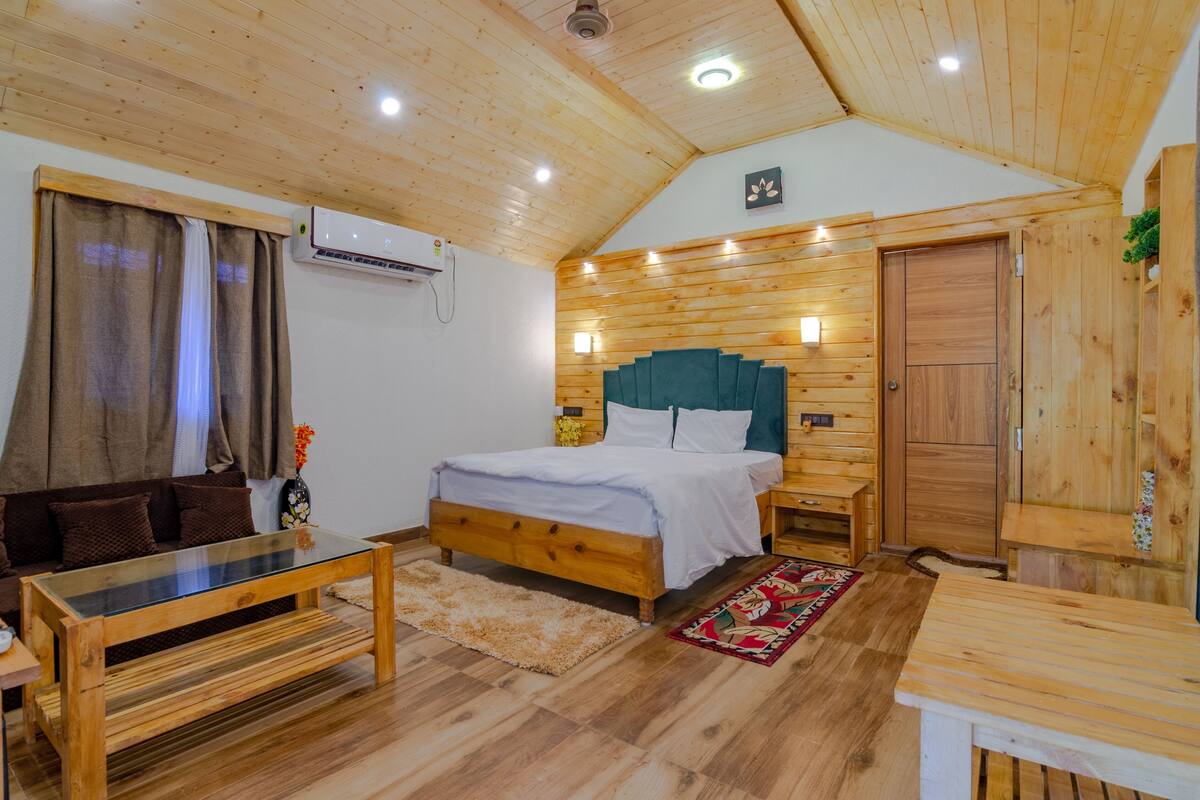 A wooden cabin-style bedroom with a bed, a wooden bench, a small table, and a nightstand.