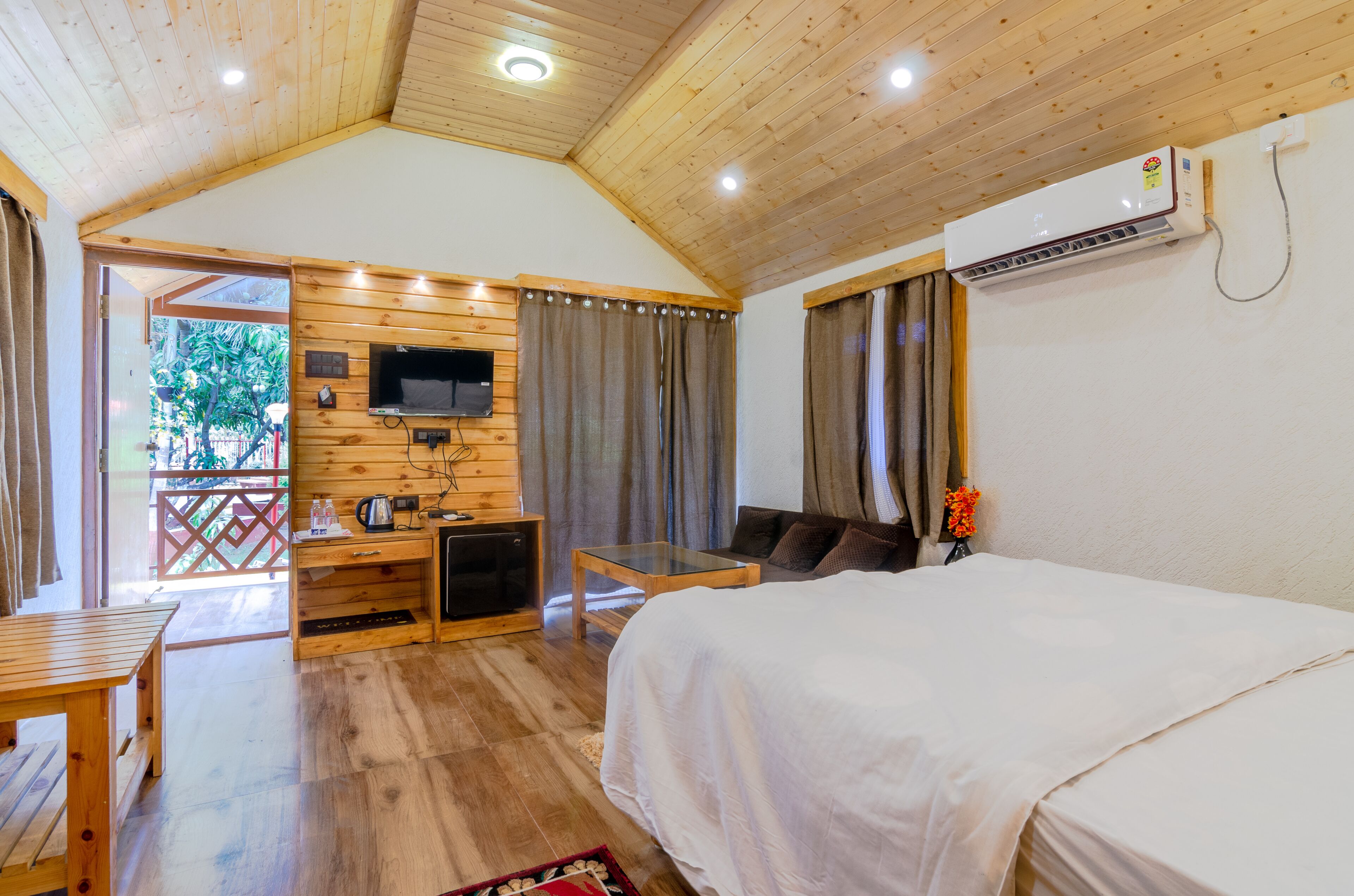A wooden-paneled room with a bed, a TV, a table, and a small seating area.