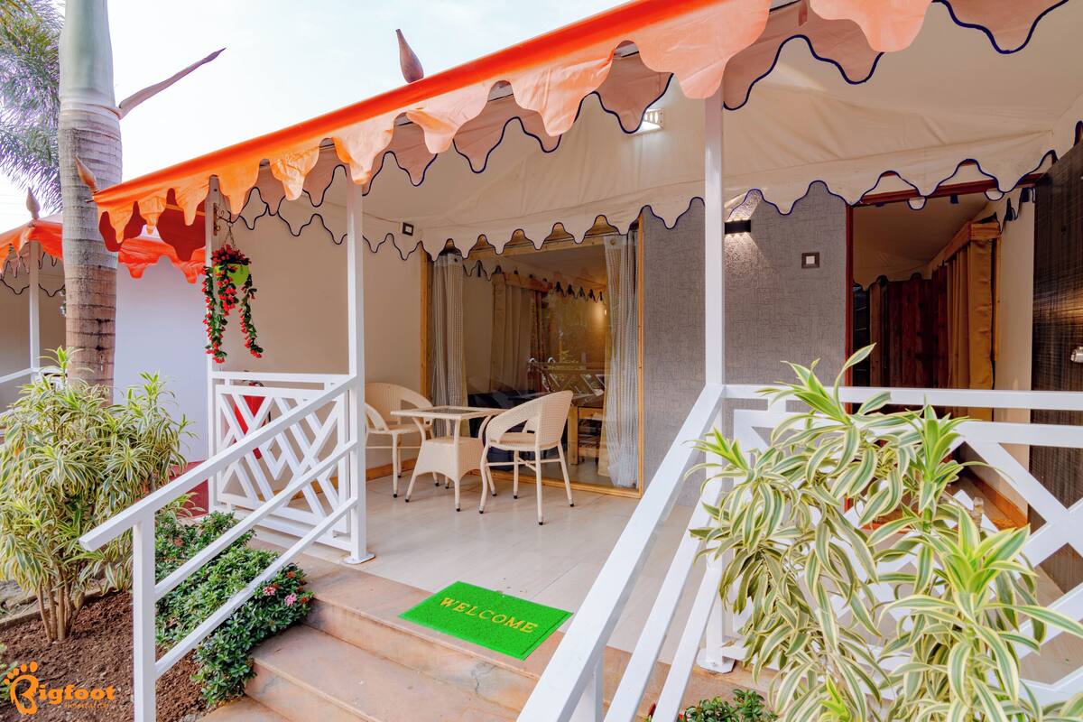 A covered outdoor seating area with a table and chairs, a welcome mat, and potted plants.