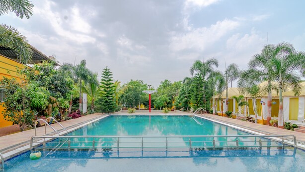 A swimming pool with a metal railing, surrounded by palm trees and a building with yellow walls.
