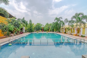 A swimming pool with a metal railing, surrounded by palm trees and a building with yellow walls. - Natures Dreamland Holiday Resort (Igatpuri)